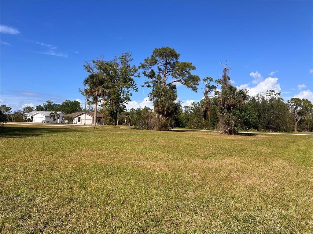 A grassy, vacant lot features several mature trees under a clear blue sky — 16810 ACAPULCO ROAD, PUNTA GORDA, FL