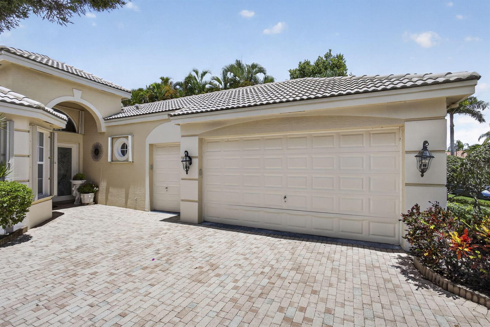 The exterior of a house features a paved driveway, a two-car garage, and landscaping — 10880 Northgreen Drive, Lake Worth FL 33449, LAKE WORTH, FL