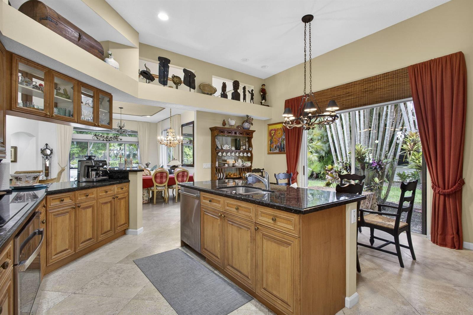 A kitchen with wood cabinets, granite countertops, and an island overlooks a dining area — 10880 Northgreen Drive, Lake Worth FL 33449, LAKE WORTH, FL