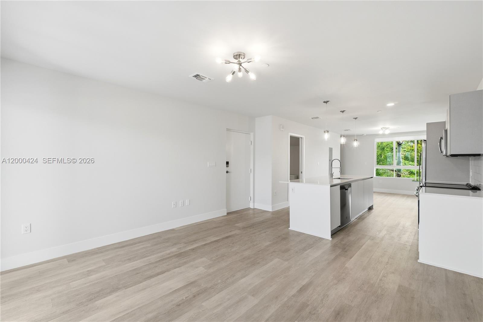 A modern, open-concept kitchen and living area features white cabinetry, a kitchen island, and light-toned flooring — 2505 NE 193rd St # 4215, Miami FL 33180, MIAMI, FL