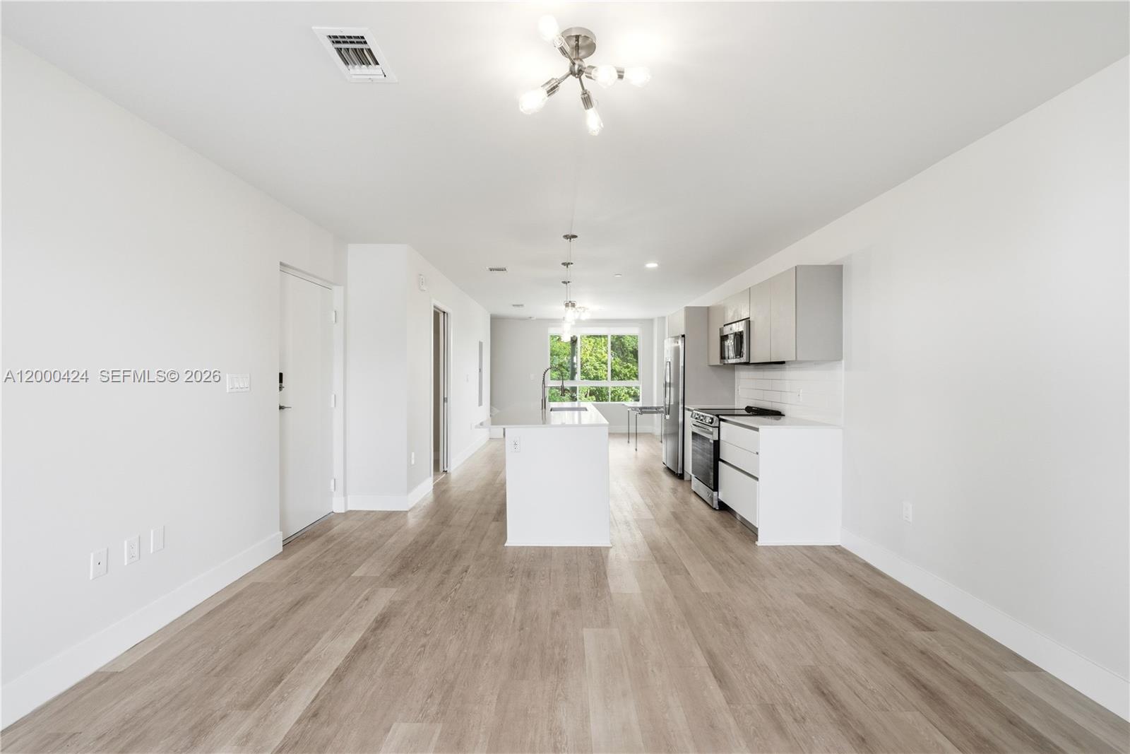 A modern kitchen features white cabinetry, a central island, and light wood-look flooring — 2505 NE 193rd St # 4215, Miami FL 33180, MIAMI, FL