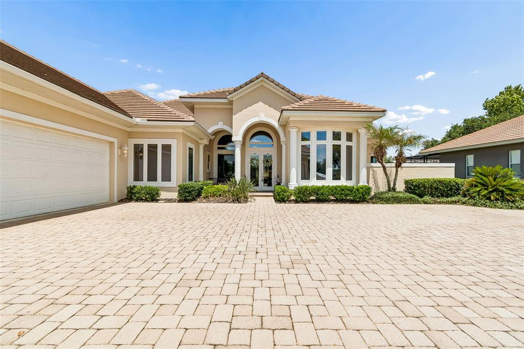 A beige single-story house with a paved driveway, arched entryway, and a multi-car garage — 12749 GRAND TRAVERSE DRIVE, DADE CITY, FL
