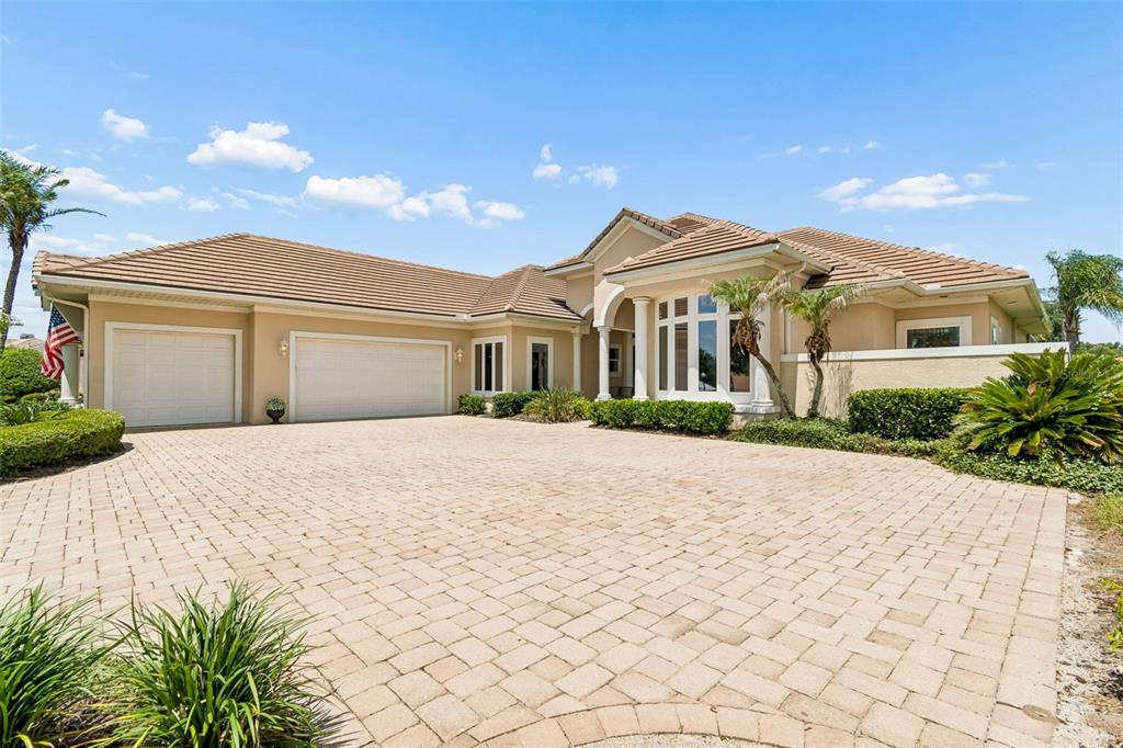 A single-story house with a beige stucco exterior, tiled roof, and a large paver driveway — 12749 GRAND TRAVERSE DRIVE, DADE CITY, FL