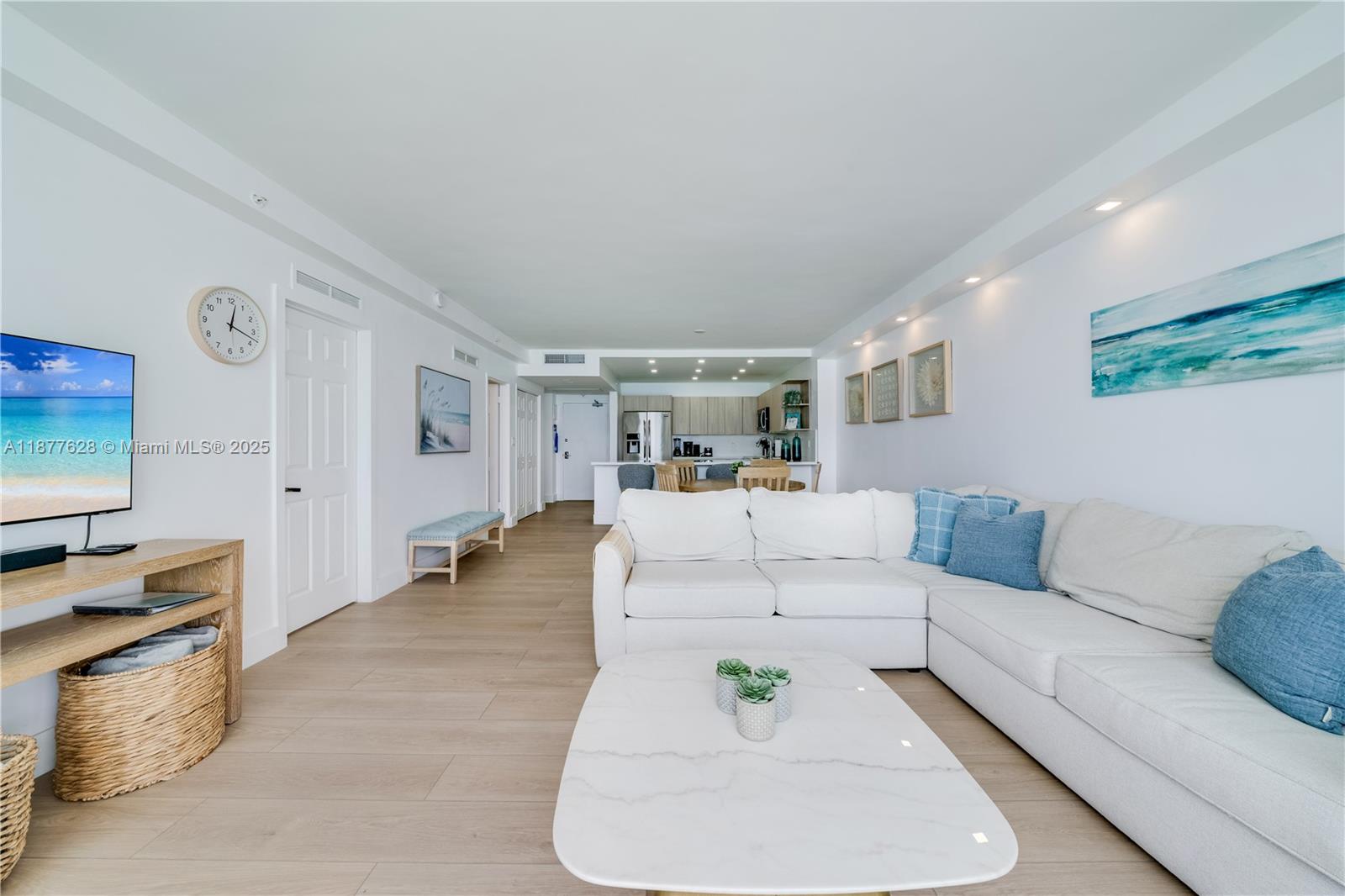 A living room features a white sectional sofa, marble coffee table, and open kitchen area — 5601 Collins Ave # 1011, Miami Beach FL 33140, MIAMI BEACH, FL