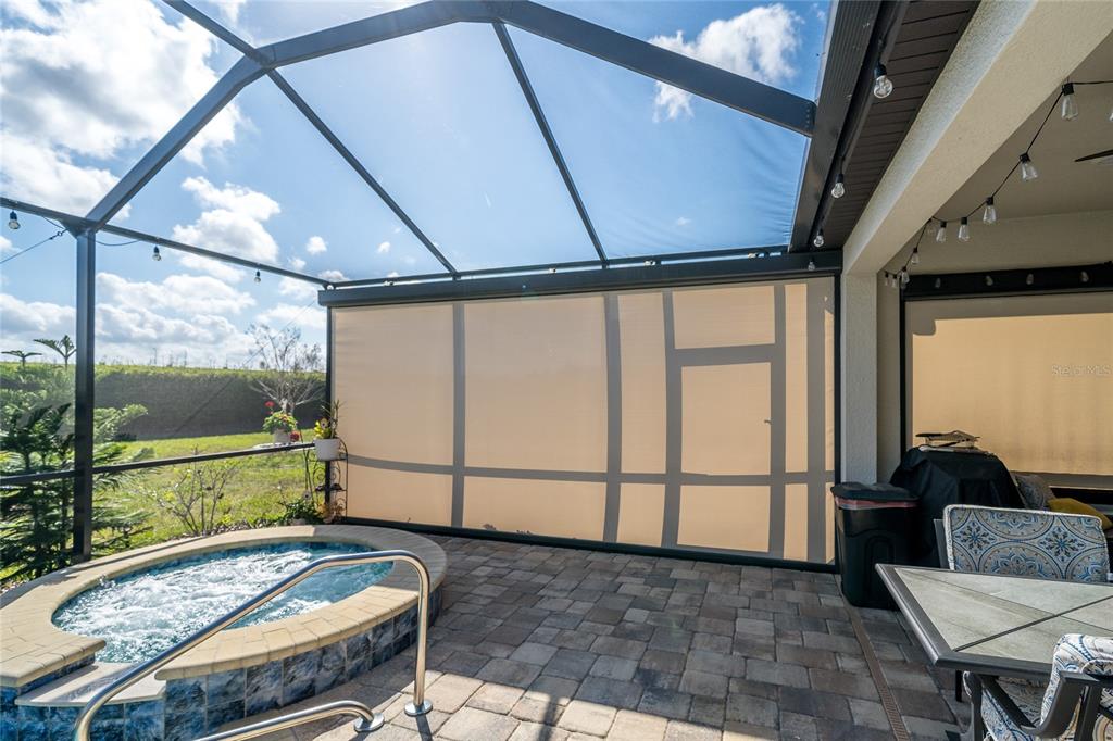 A screened-in patio features a hot tub, stone pavers, and retractable privacy shades — 4748 BALLAST CREST COVE, LAND O LAKES, FL