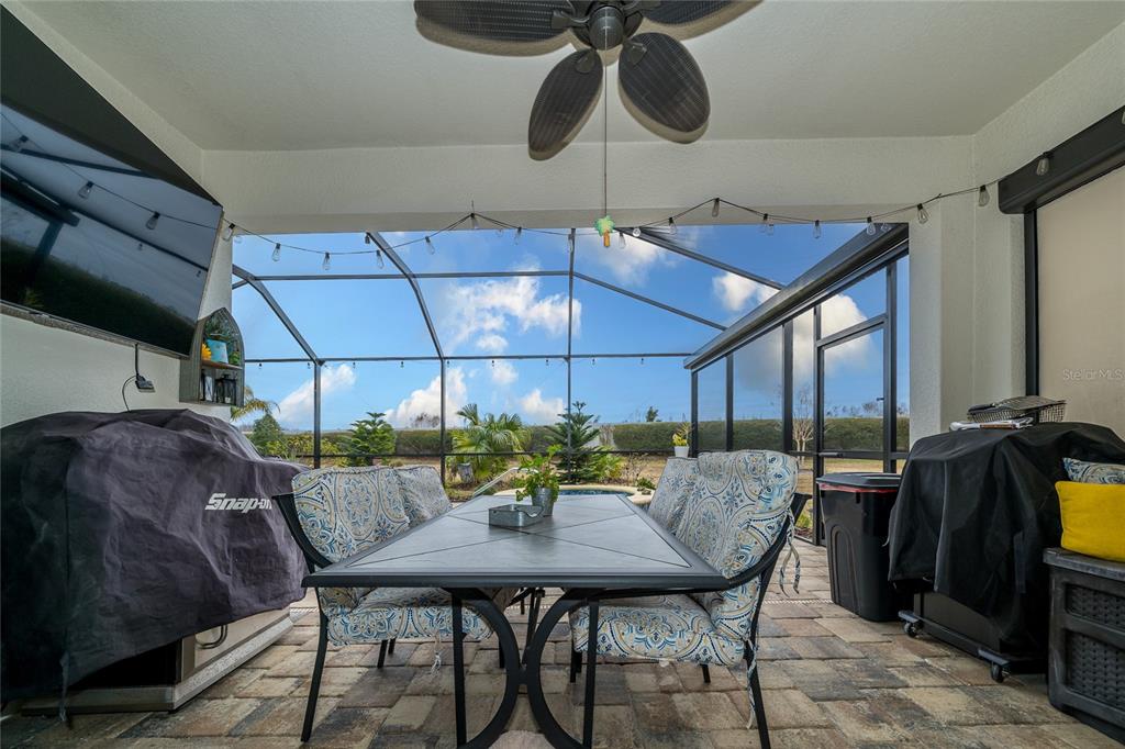A covered patio features a dining set, a ceiling fan, and a screened pool enclosure — 4748 BALLAST CREST COVE, LAND O LAKES, FL