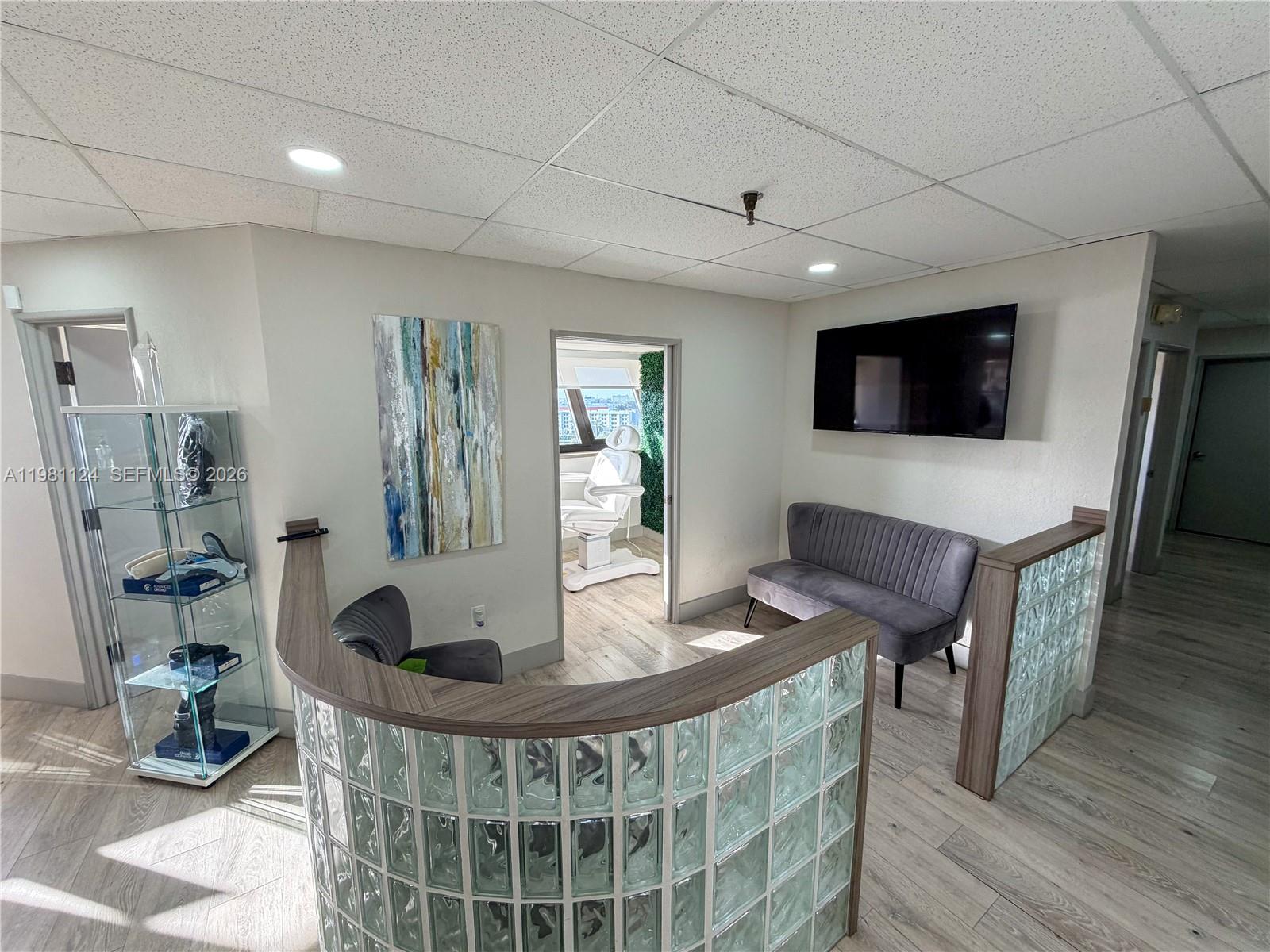 A waiting area features a glass block reception desk, gray seating, and a wall-mounted television — 7100 W 20th Ave # 616, Hialeah FL 33016, HIALEAH, FL