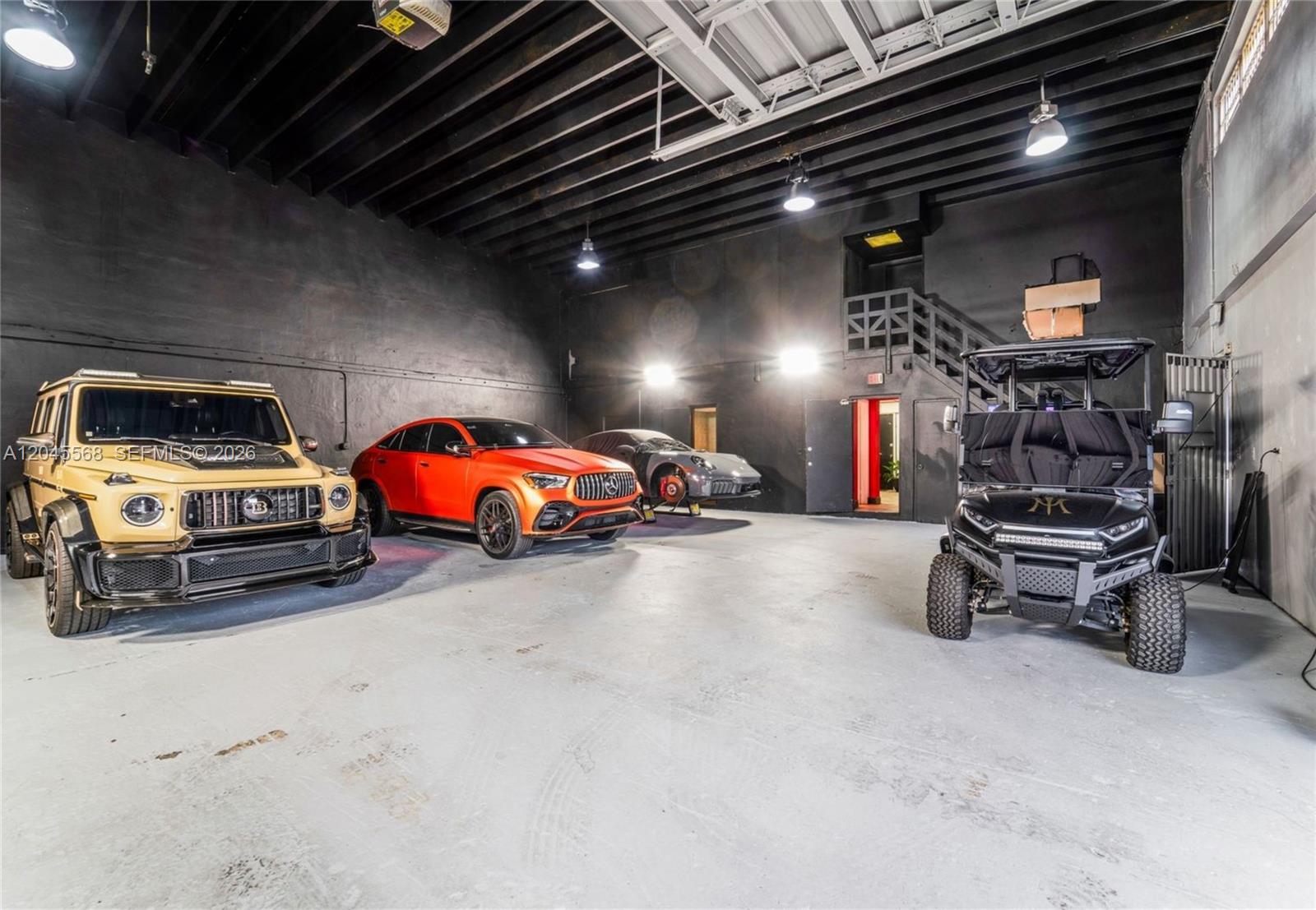 A spacious garage with black walls, exposed ceiling beams, and several luxury vehicles parked inside — 5571 NW 84th Ave, Doral FL 33166, DORAL, FL
