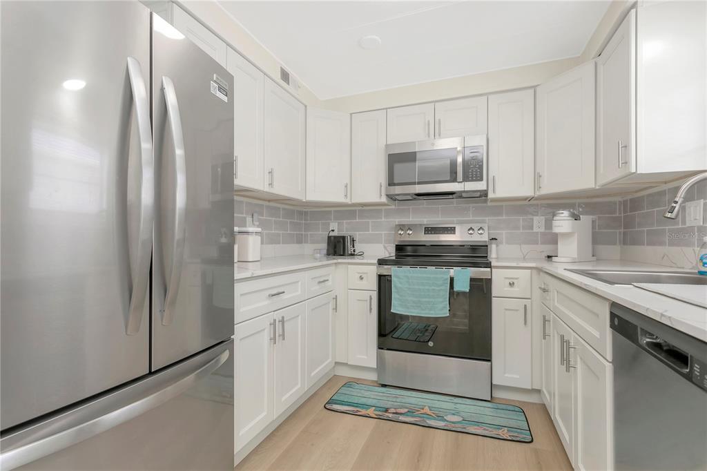 A kitchen with white cabinets, stainless steel appliances, and a gray subway tile backsplash — 115 WHITE OAK WAY, SARASOTA, FL