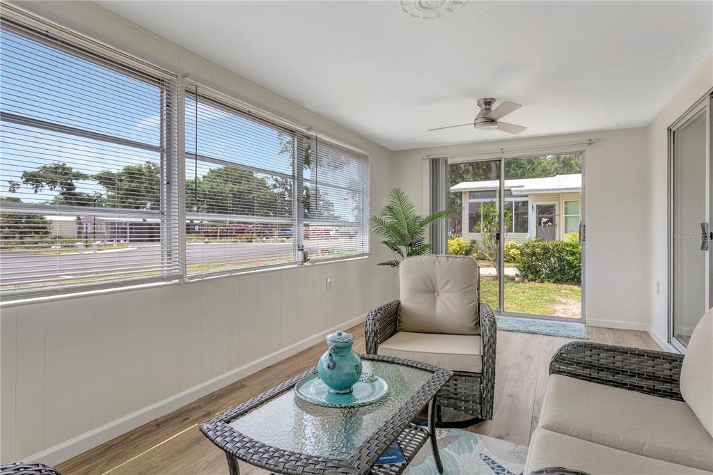A sunroom with light wood-look flooring, wicker furniture, and large windows overlooking a neighborhood street — 115 WHITE OAK WAY, SARASOTA, FL