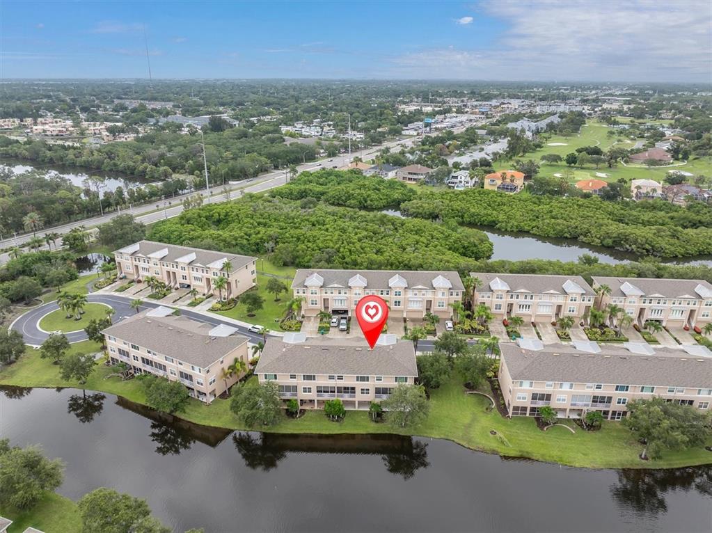 An aerial view shows several multi-story townhome buildings situated along a lake and green space — 7276 ISLAMORADA CIRCLE, SEMINOLE, FL