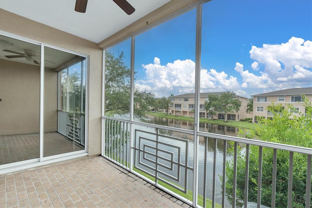 A screened-in balcony with brick flooring overlooks a pond and neighboring apartment buildings — 7276 ISLAMORADA CIRCLE, SEMINOLE, FL