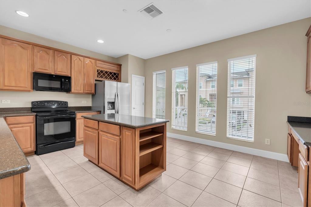 A kitchen features wood cabinets, black appliances, a central island, and three tall windows — 7276 ISLAMORADA CIRCLE, SEMINOLE, FL