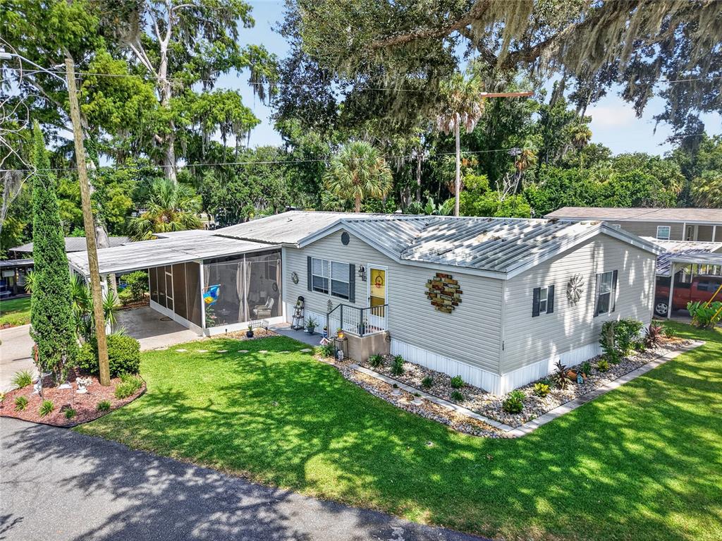 A single-story manufactured home features a screened-in carport and a landscaped front yard — 704 KIMBERLY AVENUE, LEESBURG, FL