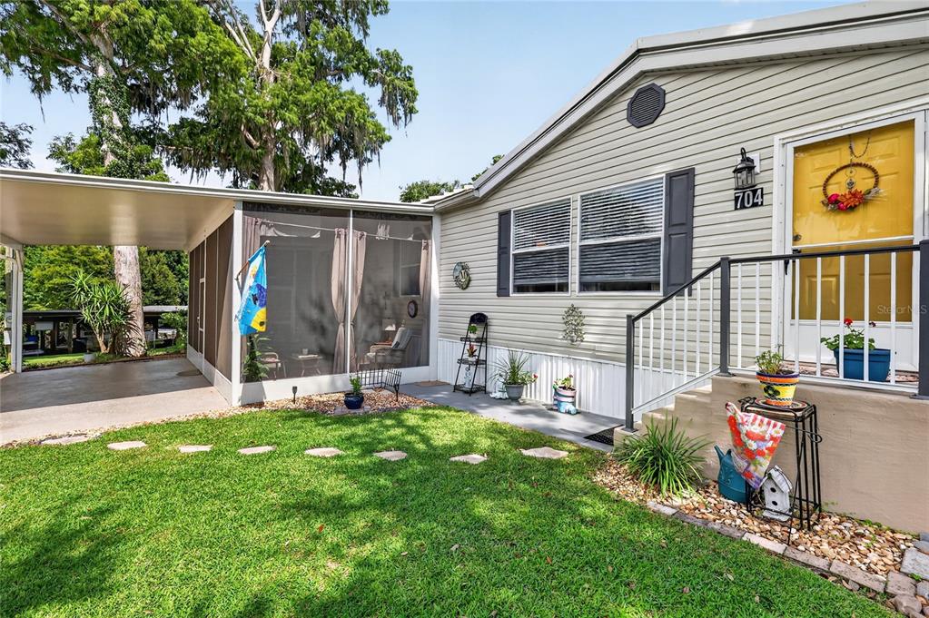 A light-colored mobile home features a screened-in porch, a carport, and a bright yellow front door — 704 KIMBERLY AVENUE, LEESBURG, FL