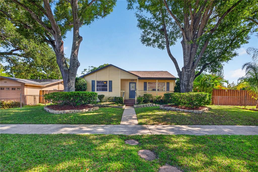 A yellow single-story house with a front walkway, two large trees, and landscaped garden beds — 6113 10TH AVENUE S, GULFPORT, FL
