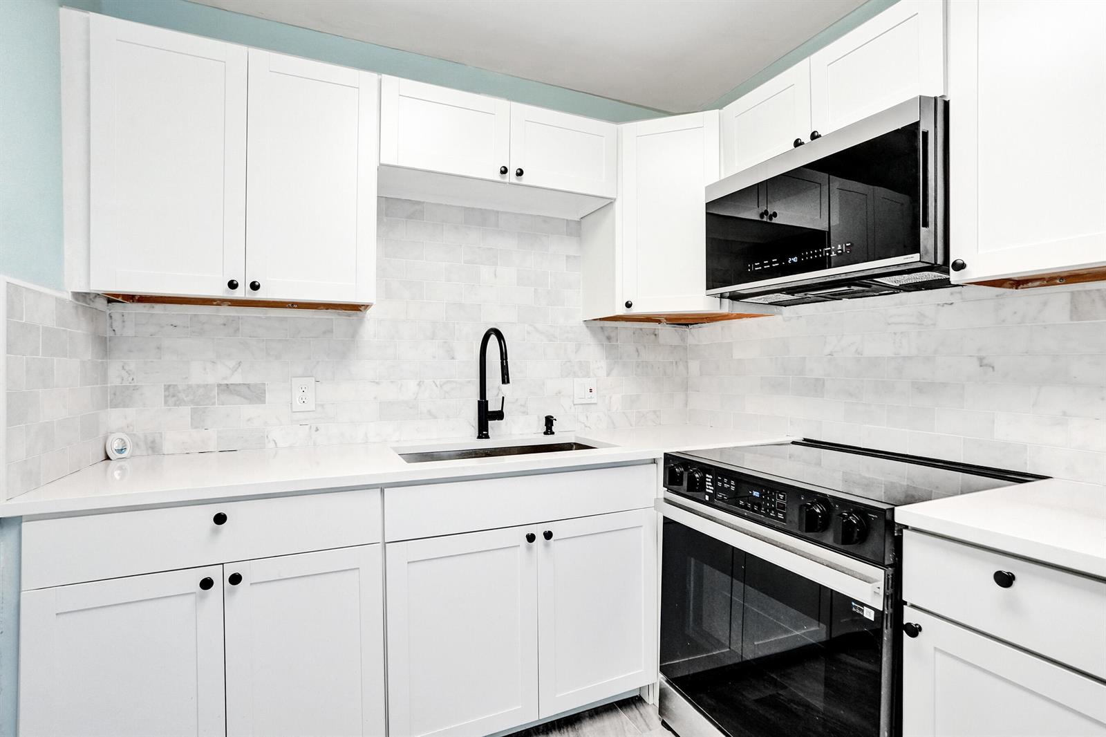 A kitchen features white cabinets, marble tile backsplash, quartz countertops, and black appliances — 358 Oakridge T # 358, Deerfield Beach FL 33442, DEERFIELD BEACH, FL