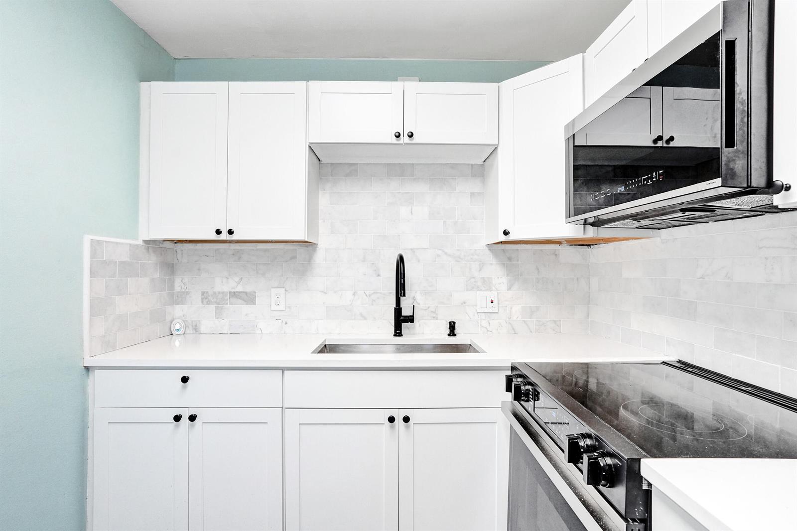 A kitchen features white cabinets, a marble subway tile backsplash, and a black faucet — 358 Oakridge T # 358, Deerfield Beach FL 33442, DEERFIELD BEACH, FL