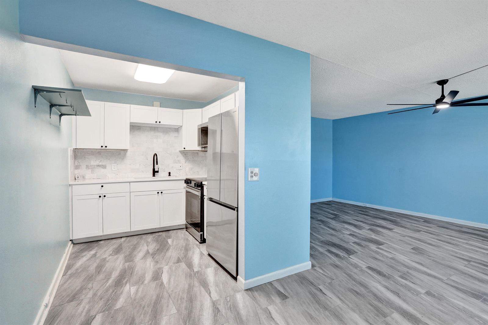 A kitchen with white cabinets and stainless steel appliances opens into a blue-walled living area — 358 Oakridge T # 358, Deerfield Beach FL 33442, DEERFIELD BEACH, FL