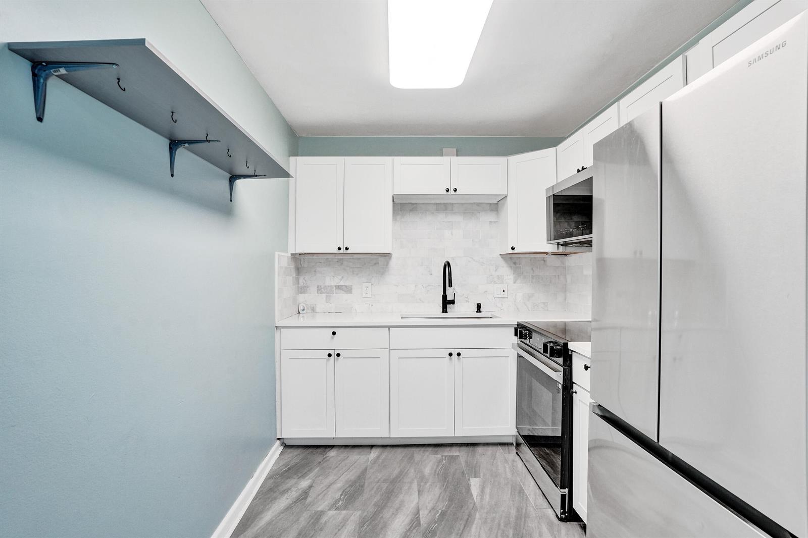A kitchen features white cabinets, a subway tile backsplash, stainless steel appliances, and a wall shelf — 358 Oakridge T # 358, Deerfield Beach FL 33442, DEERFIELD BEACH, FL