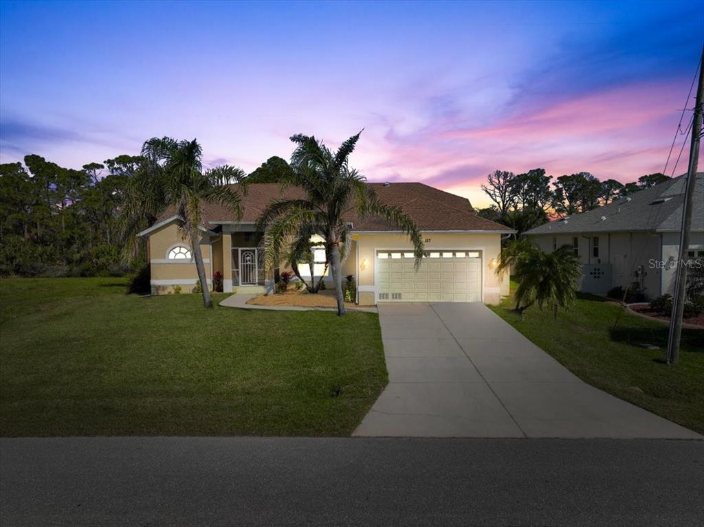 A single-story house with a two-car garage and palm trees stands under a sunset sky — 127 WHITE MARSH LANE, ROTONDA WEST, FL