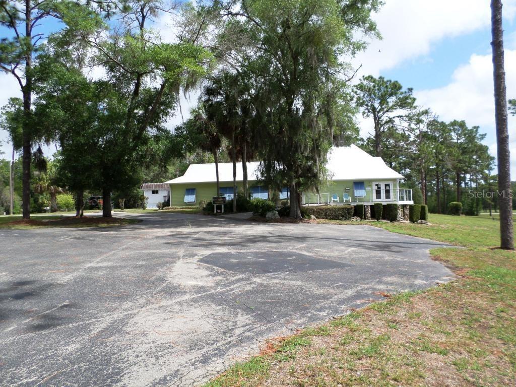 A light green building with a white roof sits behind a large, weathered asphalt parking lot — 8621 SW 200TH CIR, DUNNELLON, FL