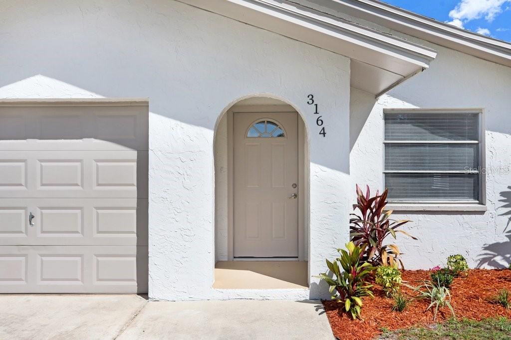 The exterior of a white house features a garage, an arched entryway, and landscaping — 3166 DOWNING STREET, CLEARWATER, FL