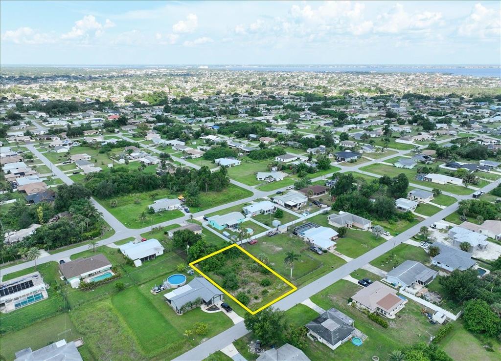 An aerial view shows a vacant, rectangular residential lot outlined in yellow within a neighborhood — 3268 PINETREE STREET, PORT CHARLOTTE, FL