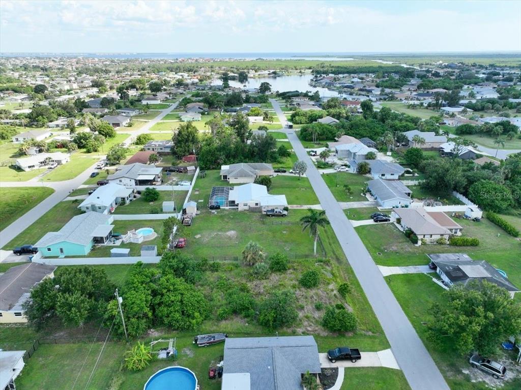 An aerial view shows a suburban neighborhood with houses, green lawns, and a nearby lake — 3268 PINETREE STREET, PORT CHARLOTTE, FL