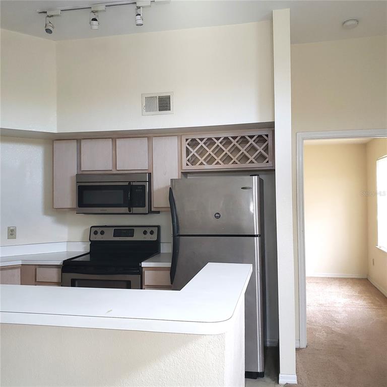 A kitchen features stainless steel appliances, light wood cabinets, and a white breakfast bar — 7300 WESTPOINTE BOULEVARD UNIT 732, ORLANDO, FL