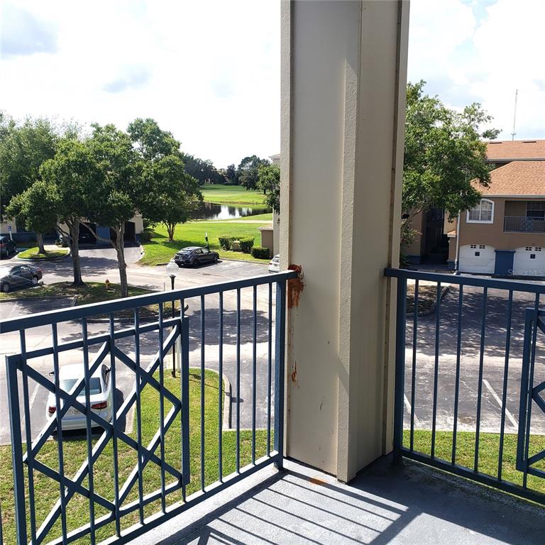 A balcony with a metal railing overlooks a parking lot, green space, and a pond — 7300 WESTPOINTE BOULEVARD UNIT 732, ORLANDO, FL