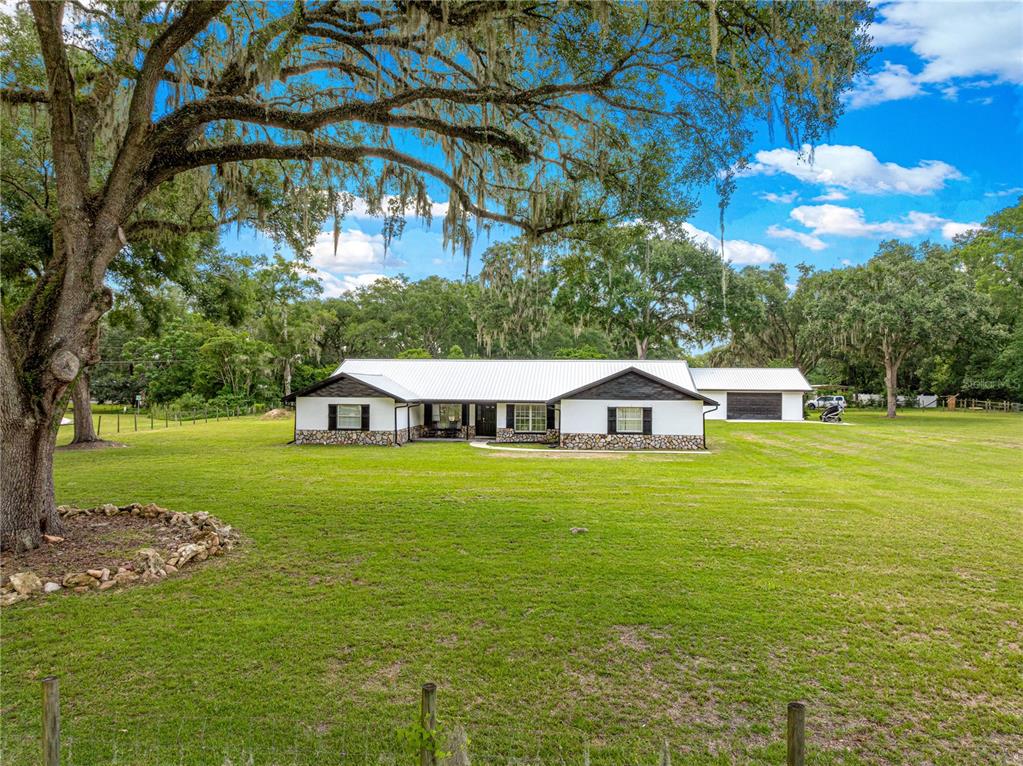 A single-story white house with a metal roof and stone accents sits on a lawn — 6575 NW 50TH AVENUE, OCALA, FL