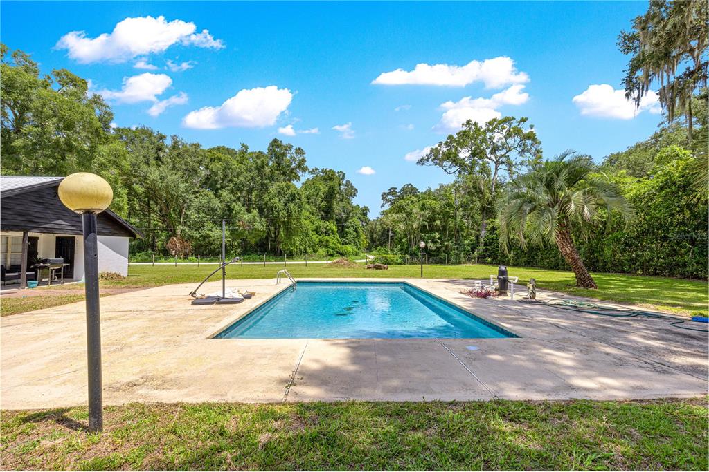 An outdoor rectangular swimming pool sits on a concrete patio next to a house — 6575 NW 50TH AVENUE, OCALA, FL