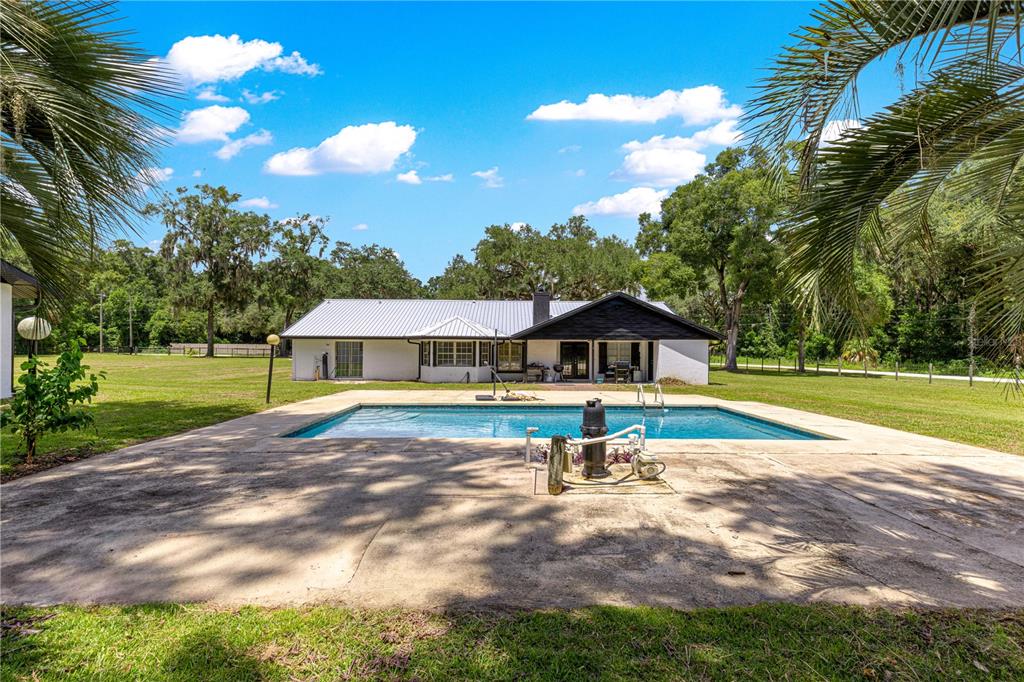 A white house with a metal roof sits behind a rectangular swimming pool and patio — 6575 NW 50TH AVENUE, OCALA, FL