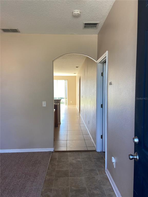 An entryway with tile flooring leads through an arched doorway toward a sunlit kitchen area — 628 MADINA CIRCLE, DAVENPORT, FL