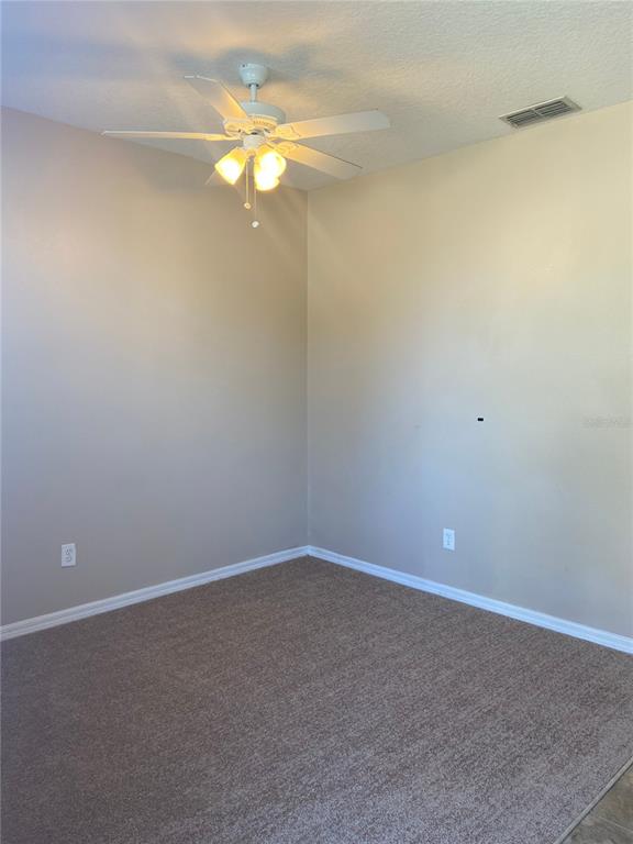 An empty bedroom features beige walls, white trim, carpeted flooring, and a ceiling fan — 628 MADINA CIRCLE, DAVENPORT, FL