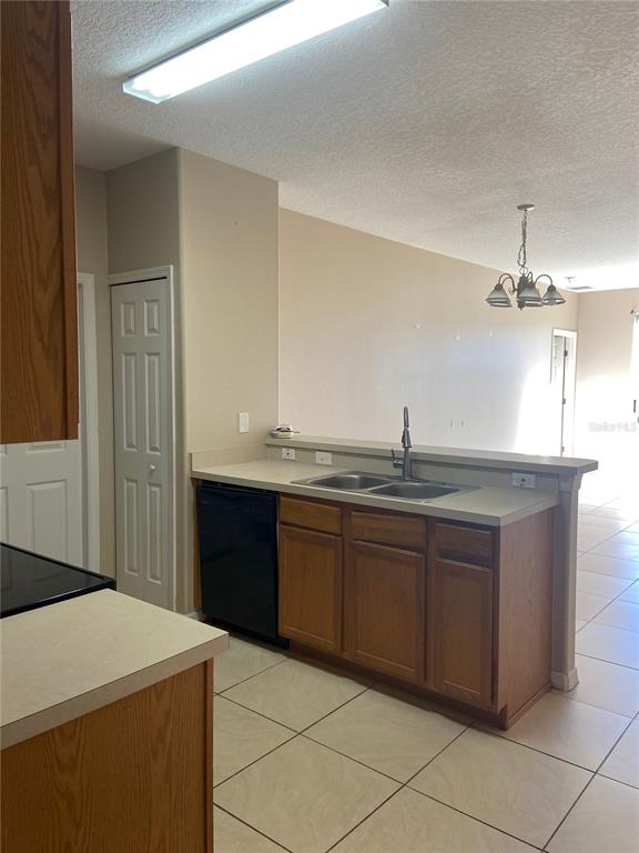 A kitchen features wood cabinets, a black dishwasher, a double sink, and tile flooring — 628 MADINA CIRCLE, DAVENPORT, FL