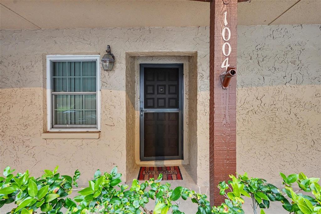 A tan stucco exterior features a front door with a screen, a window, and address numbers — 601 N HERCULES AVENUE UNIT 1004, CLEARWATER, FL