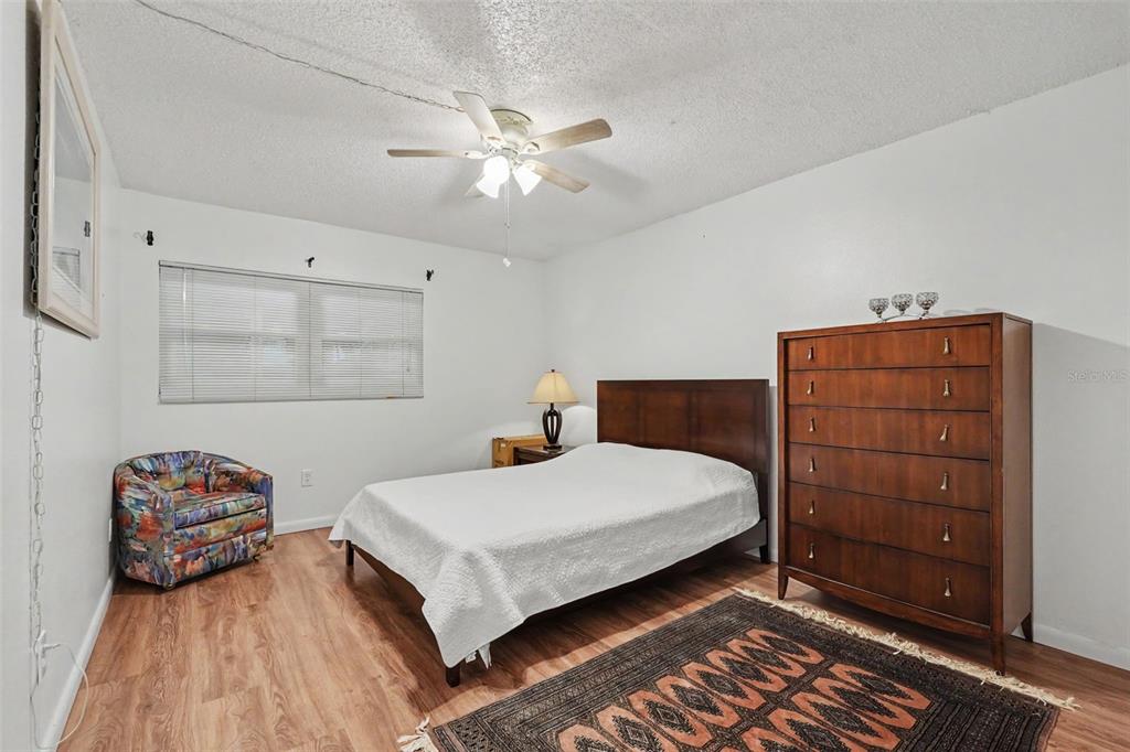 A bedroom features a bed, a tall wooden dresser, a patterned armchair, and wood-look flooring — 601 N HERCULES AVENUE UNIT 1004, CLEARWATER, FL