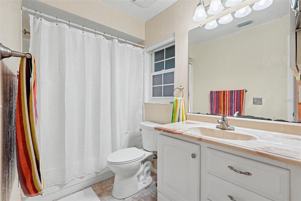 A bathroom features a white vanity, a toilet, a shower with a curtain, and a mirror — 601 N HERCULES AVENUE UNIT 1004, CLEARWATER, FL
