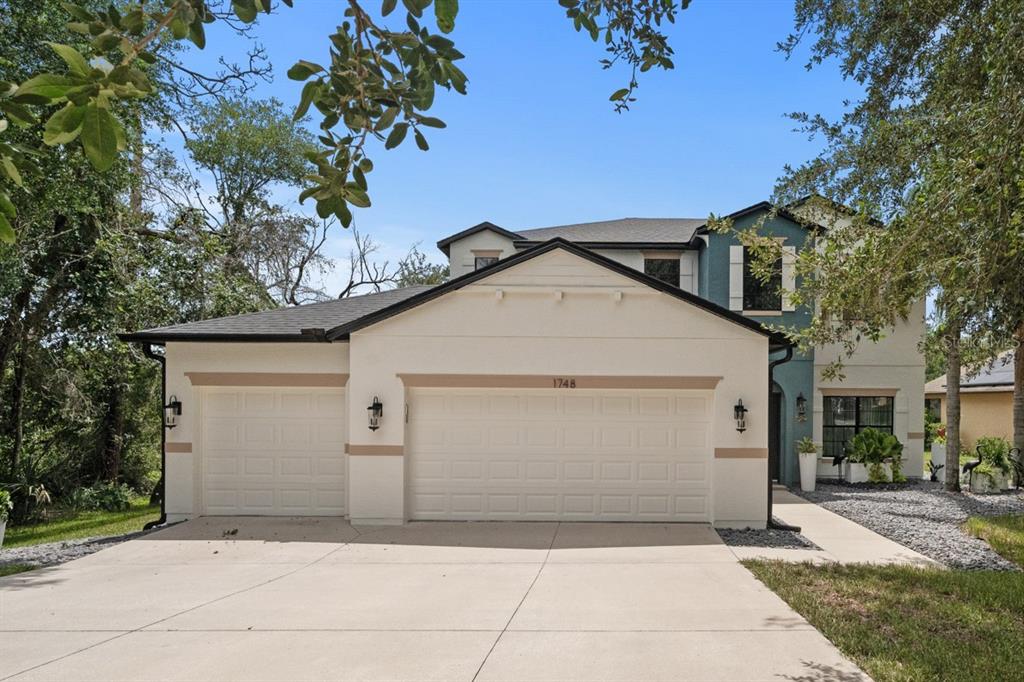 A two-story house with a three-car garage, beige stucco exterior, and a concrete driveway — 1748 WATERSIDE OAKS DRIVE, ORANGE CITY, FL
