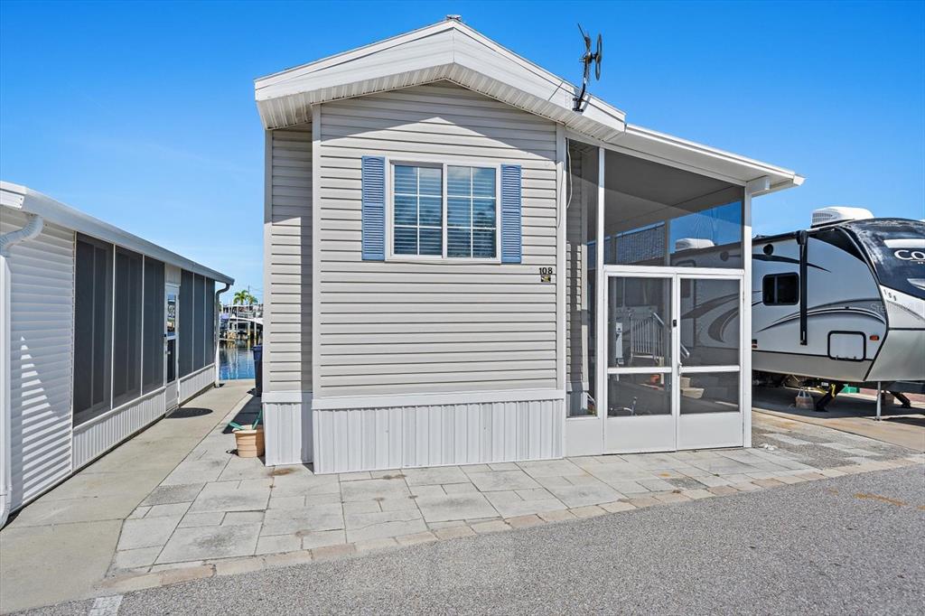 A light-colored mobile home with blue shutters and a screened-in porch sits on a paved lot — 108 BAHIA DRIVE, PALMETTO, FL