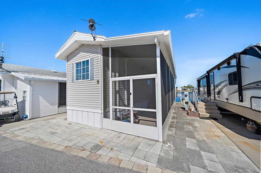 A light-colored mobile home with a screened-in porch sits on a paved lot near water — 108 BAHIA DRIVE, PALMETTO, FL