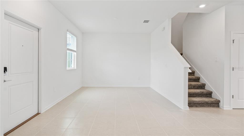 An empty room with white walls, tile flooring, a staircase, and a front door — 2204 RED SUN STREET, APOPKA, FL