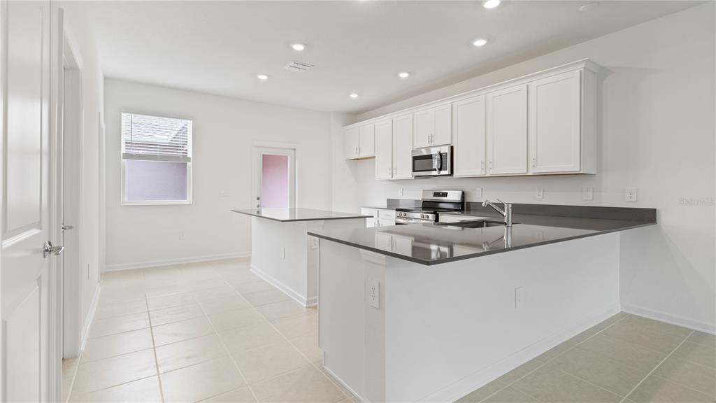 A kitchen features white cabinets, dark countertops, a kitchen island, and light tile flooring — 2204 RED SUN STREET, APOPKA, FL