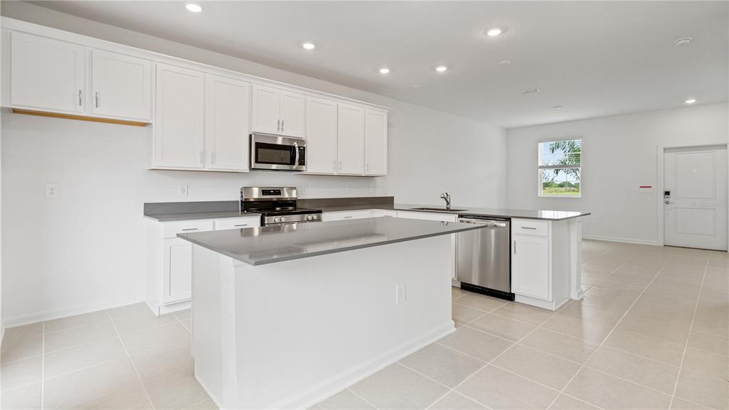 A modern kitchen features white cabinets, stainless steel appliances, a gray island, and tile flooring — 2204 RED SUN STREET, APOPKA, FL