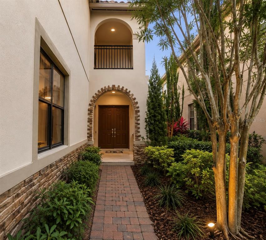 A brick walkway leads to a double-door entrance framed by a stone archway and balcony — 10359 HENBURY STREET, ORLANDO, FL