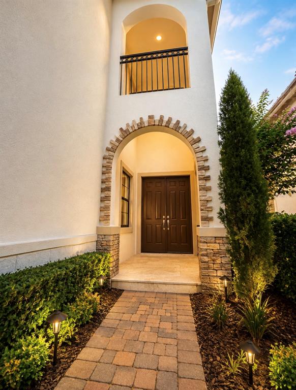 A stone-arched entryway leads to dark double doors with a balcony above — 10359 HENBURY STREET, ORLANDO, FL