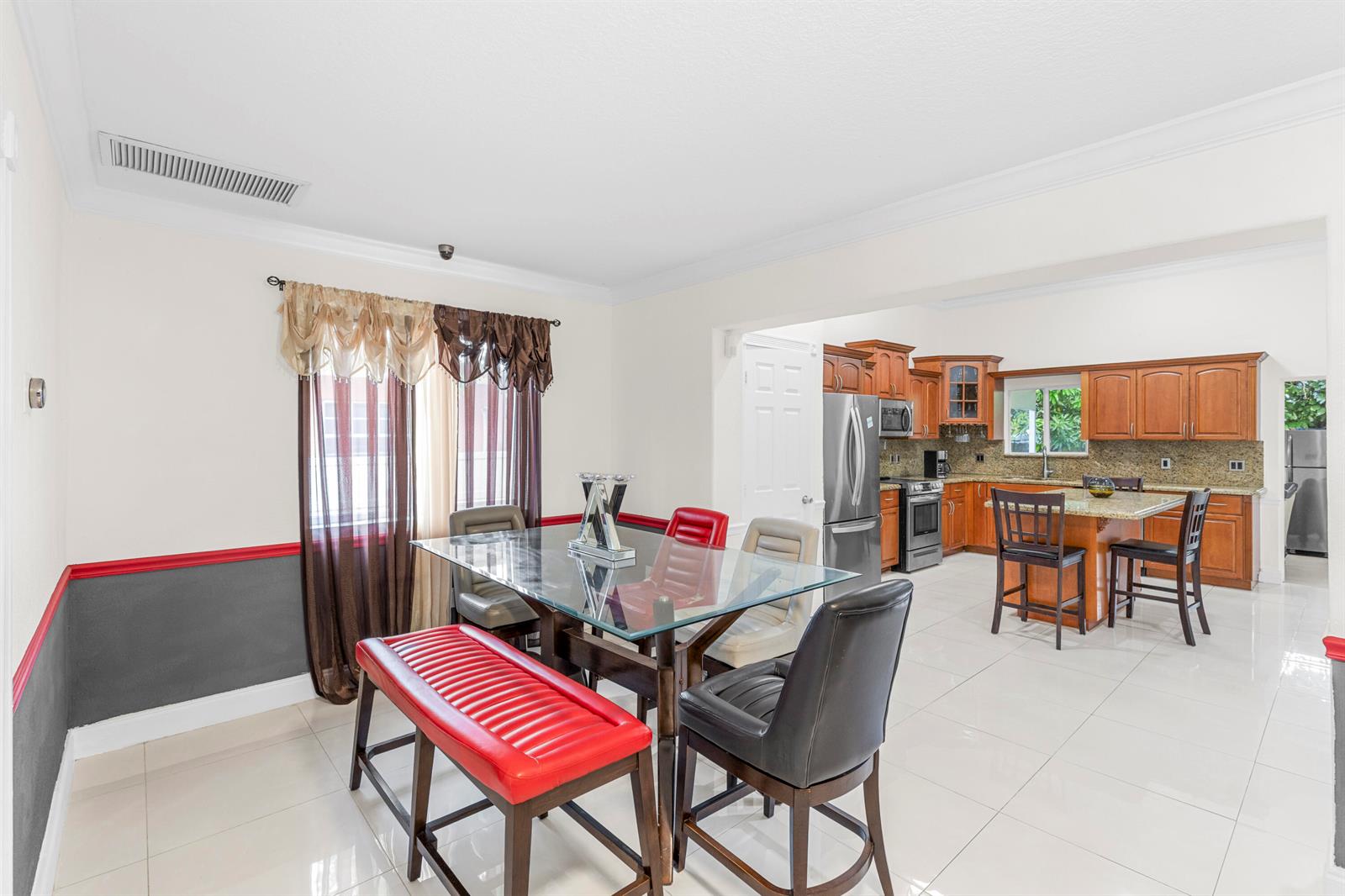 A dining area with a glass table and mixed-color chairs opens into a wood-cabinet kitchen — 321 N 72nd Terrace, Hollywood FL 33024, HOLLYWOOD, FL