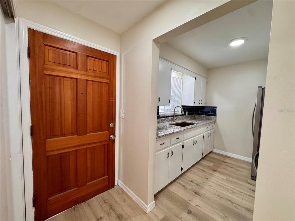 A wooden front door opens into a kitchen with white cabinets and granite countertops — 791 LAKE AVENUE UNIT 2, CLERMONT, FL